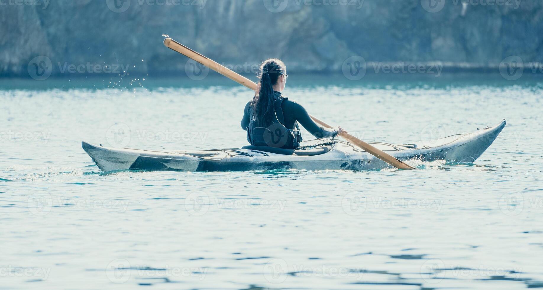 Woman sea kayak. Happy smiling woman in kayak on ocean, paddling with wooden oar. Calm sea water and horizon in background. Active lifestyle at sea. Summer vacation. photo