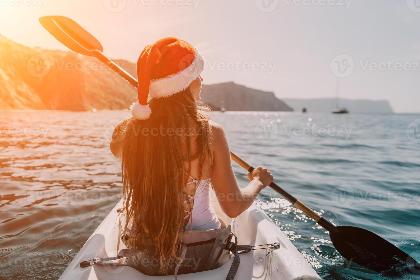 Woman in kayak back view. Happy young woman in Santa hat floating in kayak on calm sea. Summer holiday vacation and cheerful female people relaxing having fun on the boat. photo