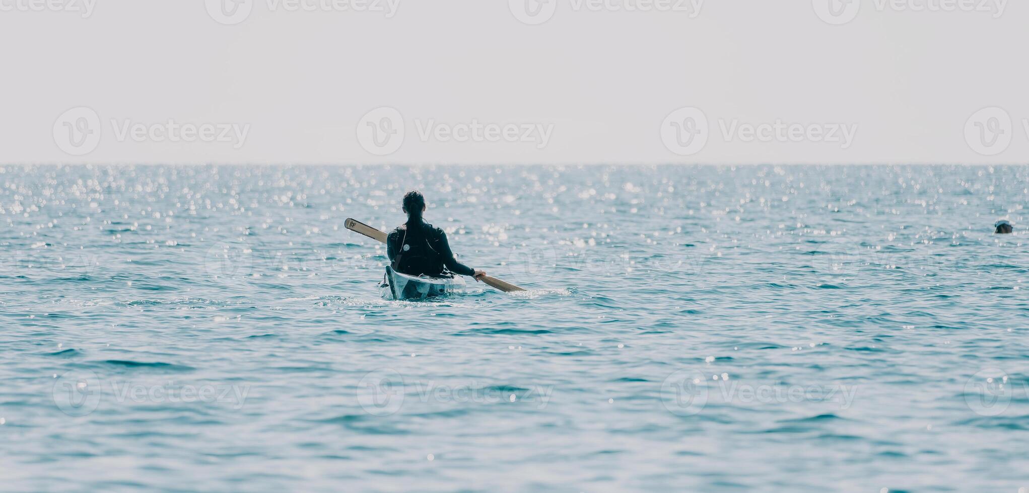 Woman sea kayak. Happy smiling woman in kayak on ocean, paddling with wooden oar. Calm sea water and horizon in background. Active lifestyle at sea. Summer vacation. photo