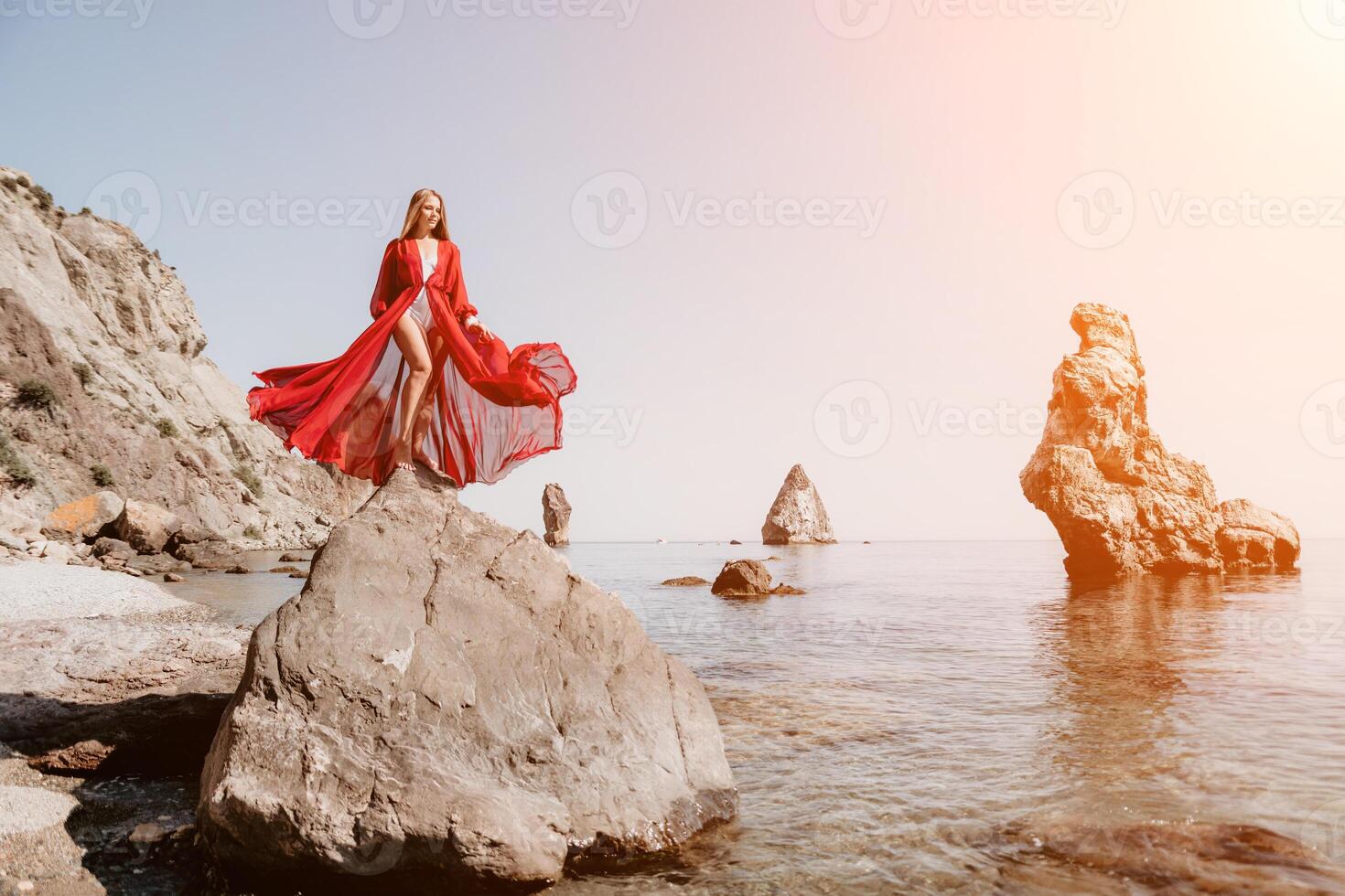 Woman travel sea. Young Happy woman in a long red dress posing on a beach near the sea on background of volcanic rocks, like in Iceland, sharing travel adventure journey photo