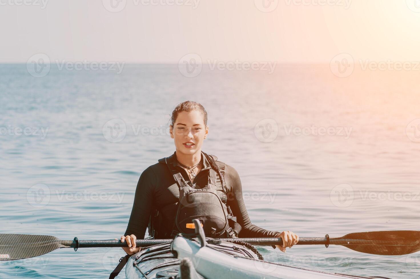 Woman sea kayak. Happy smiling woman in kayak on ocean, paddling with wooden oar. Calm sea water and horizon in background. Active lifestyle at sea. Summer vacation. photo