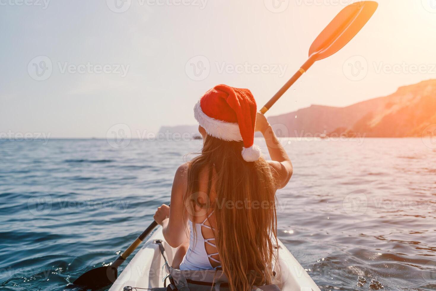 Woman in kayak back view. Happy young woman in Santa hat floating in kayak on calm sea. Summer holiday vacation and cheerful female people relaxing having fun on the boat. photo