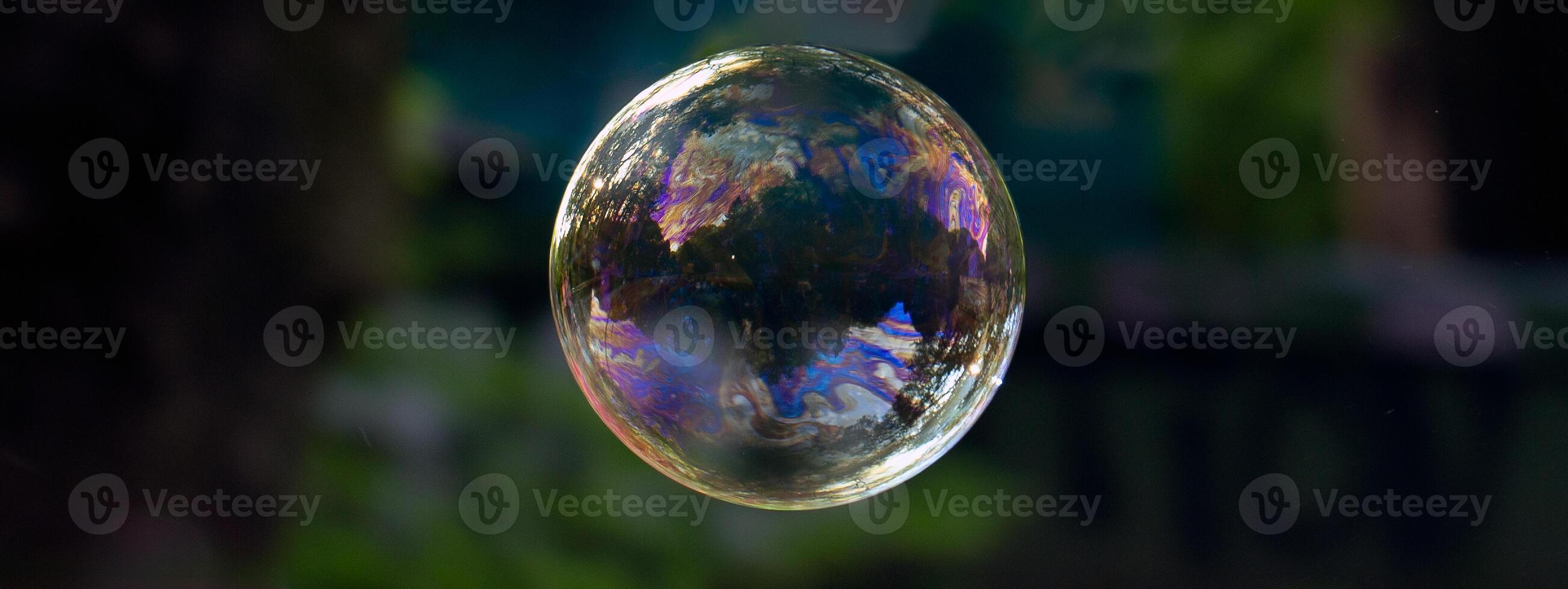 perfectly round soap bubble of a blue hue, with solar reflection and shimmer of light against a dark background photo
