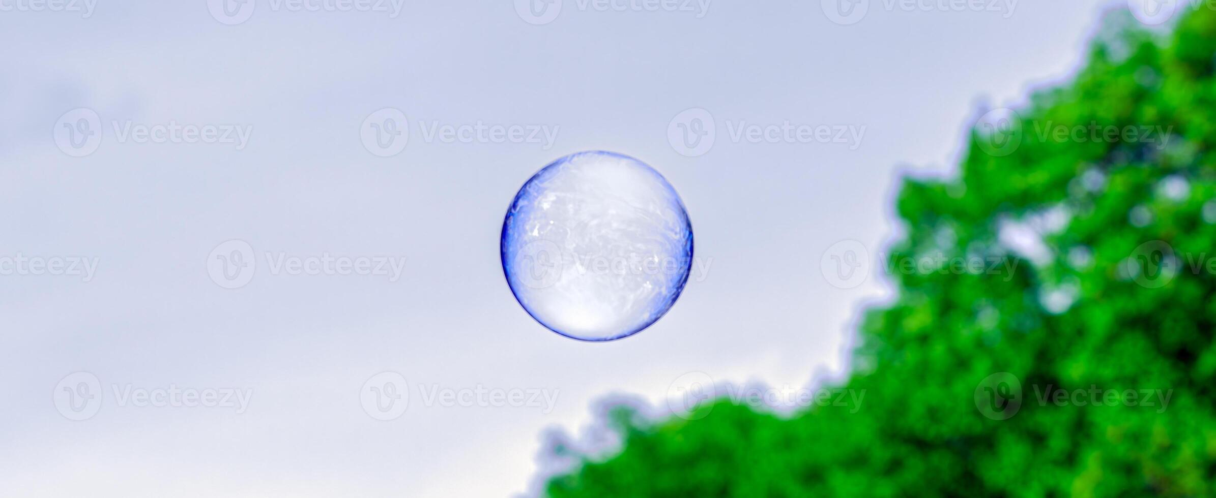 perfectly round soap bubble of a blue hue, with solar reflection and shimmer of light against a dark background photo