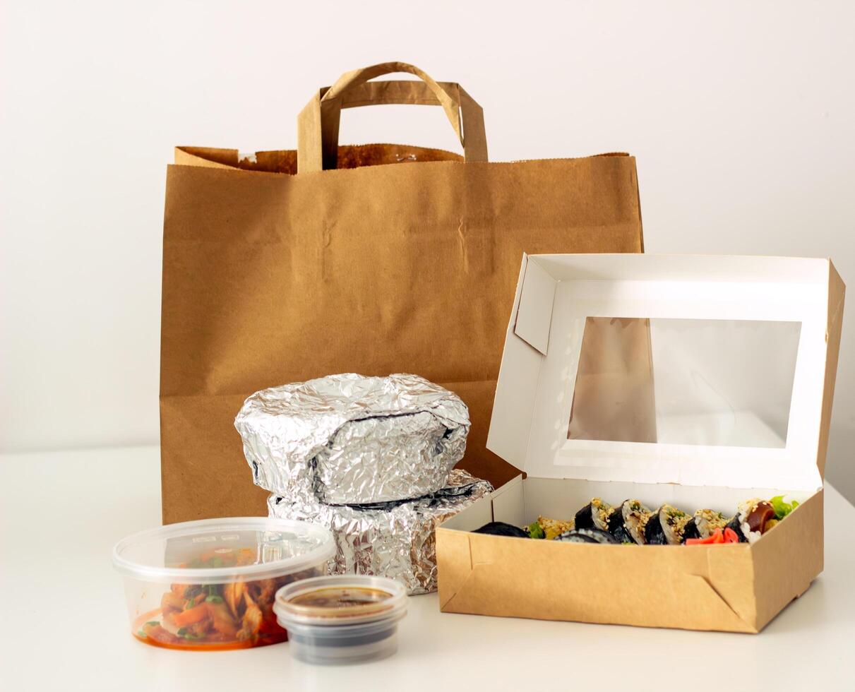 package of food from delivery stands on the table, containers with hot food packed in foil and sushi, food delivery concept photo