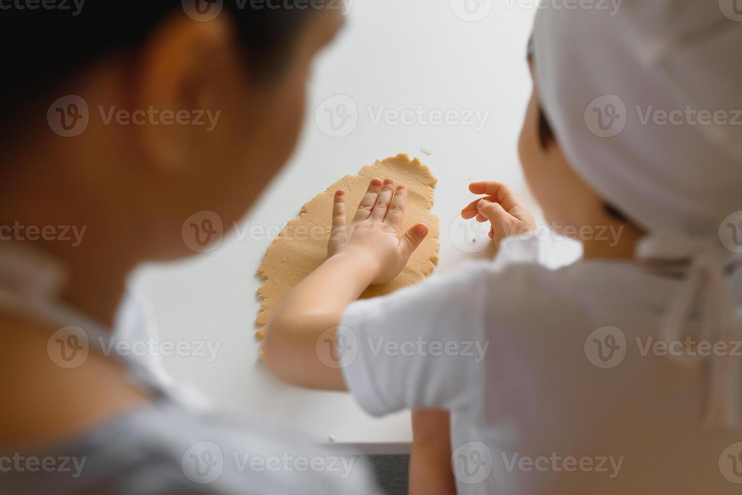 Little boy helping his mother with the baking in the kitchen standing at the counter alongside her kneading the dough for the pie photo