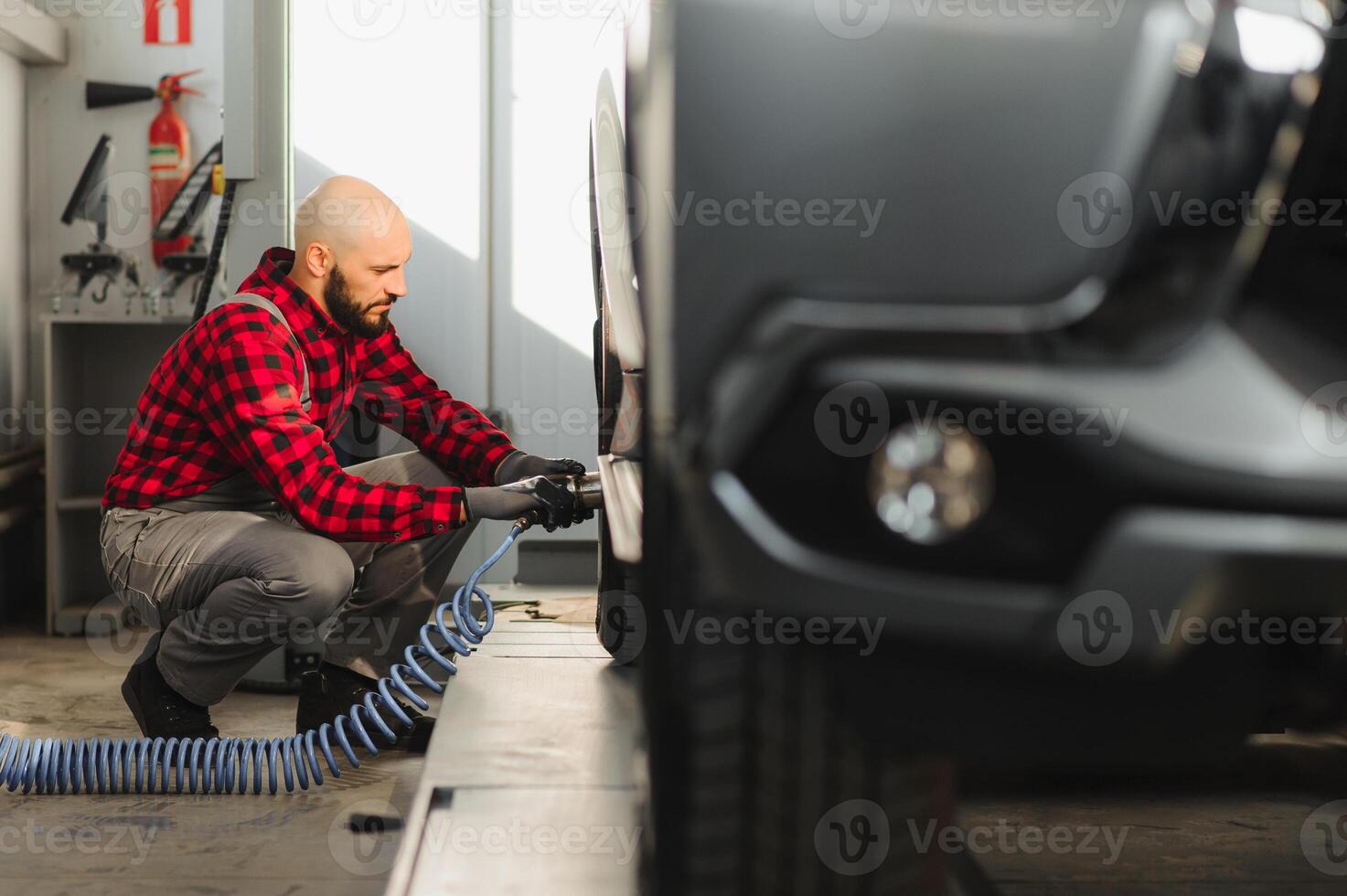 car mechanic screwing or unscrewing car wheel of lifted automobile by pneumatic wrench at repair service station photo