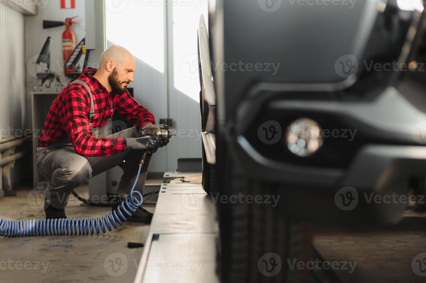 car mechanic screwing or unscrewing car wheel of lifted automobile by pneumatic wrench at repair service station photo