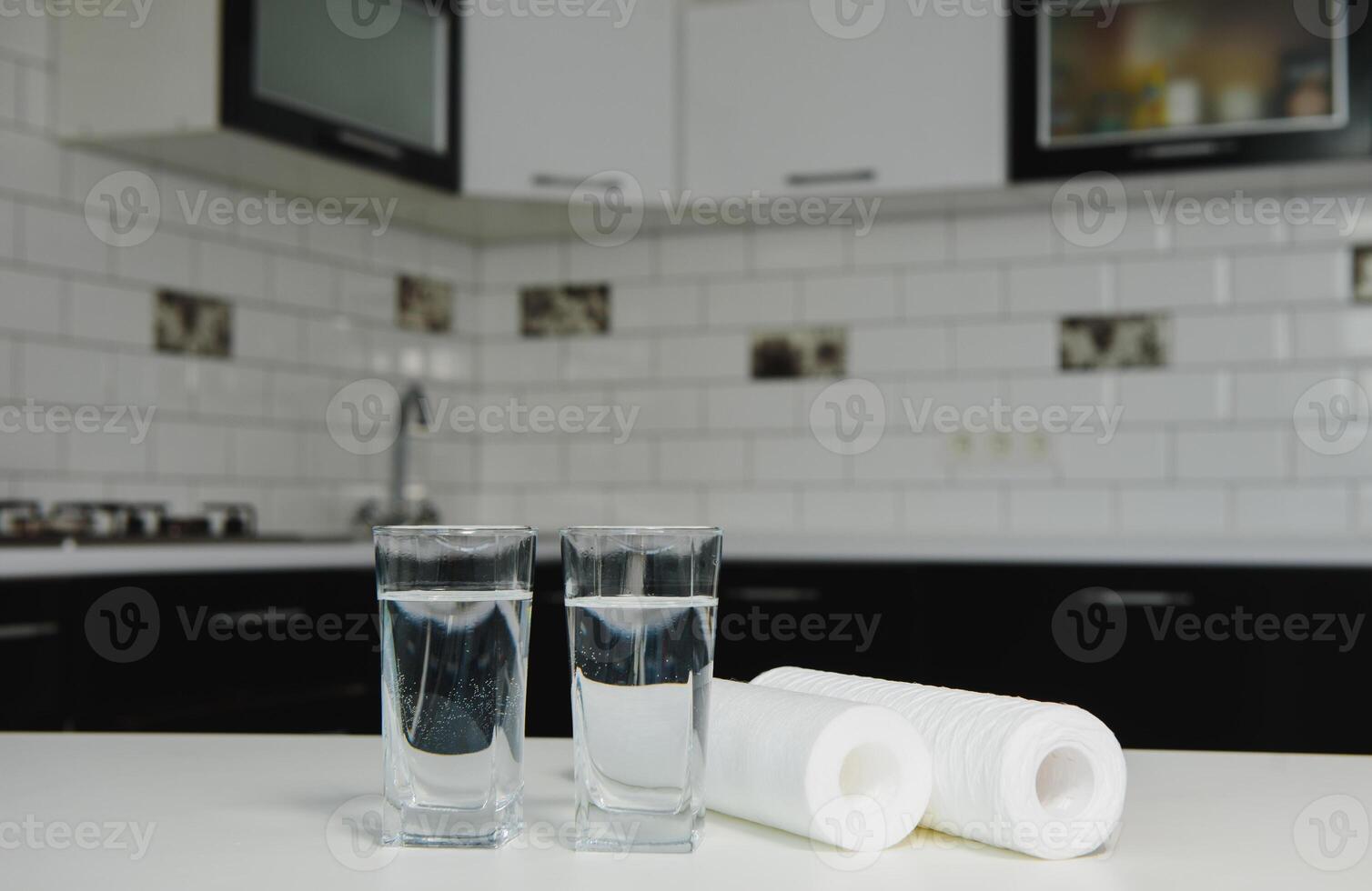 A glass of clean water with osmosis filter, green flowerpot and cartridges on white table in a kitchen interior. Concept Household filtration system. photo