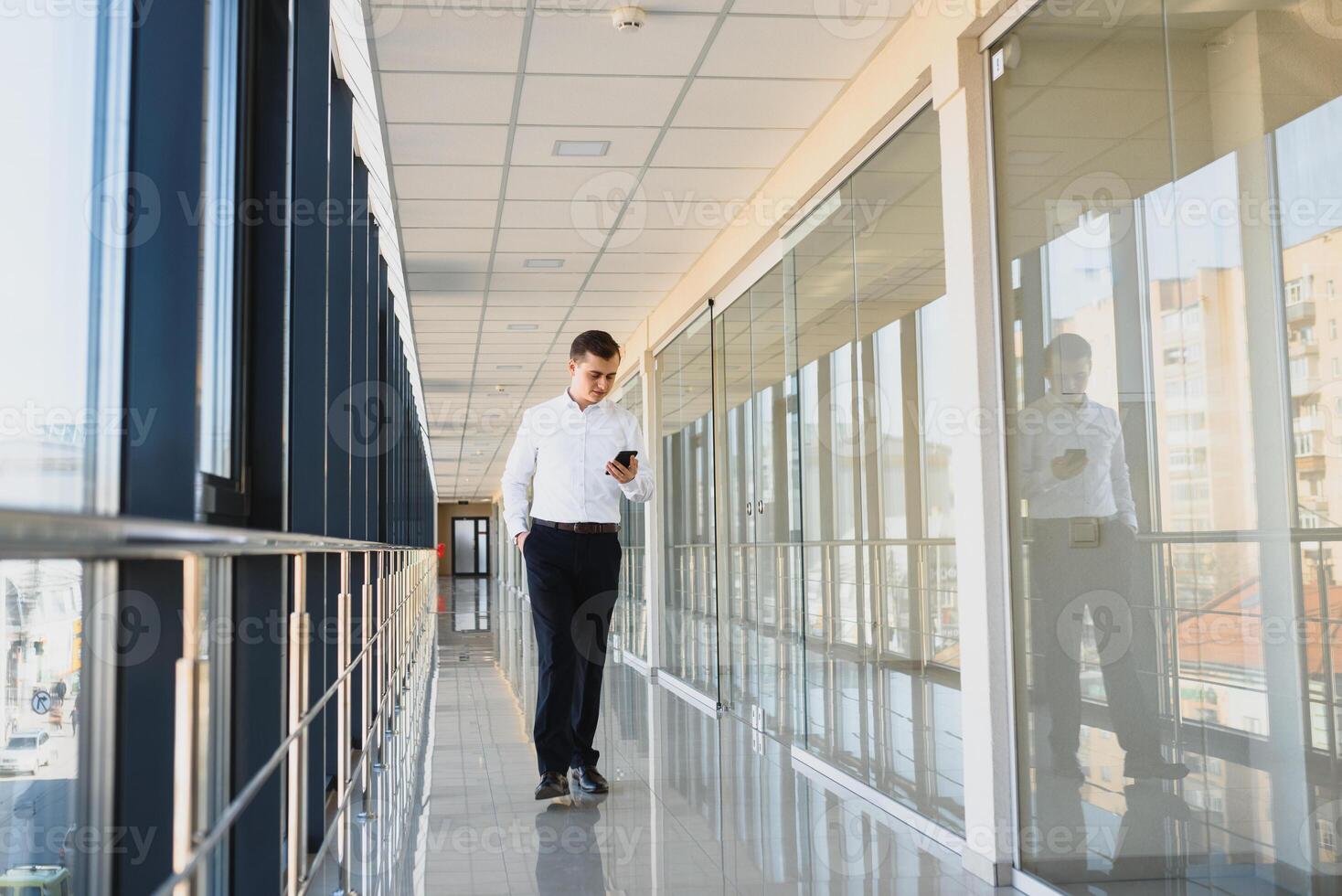 Portrait of a serious confident man boss having mobile phone conversation while resting after meeting with his partners, businessman talking on cell telephone while standing in modern space indoors photo