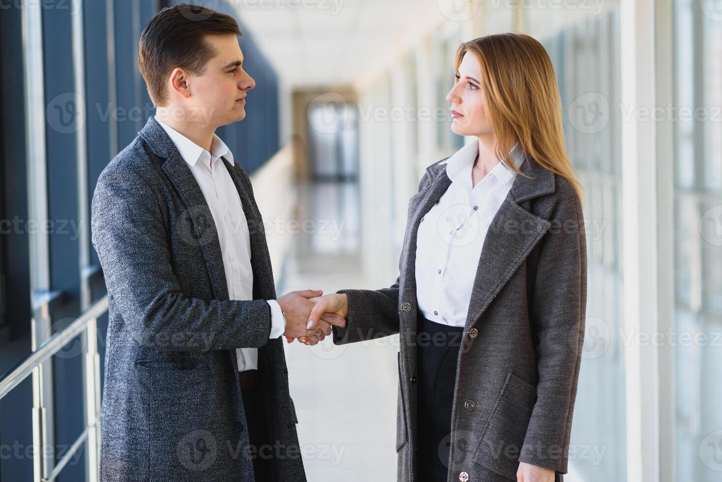 Business men and women shaking hands with a smile on the background of the large panoramic windows in a modern business center. Models dressed in a dark business suits. photo