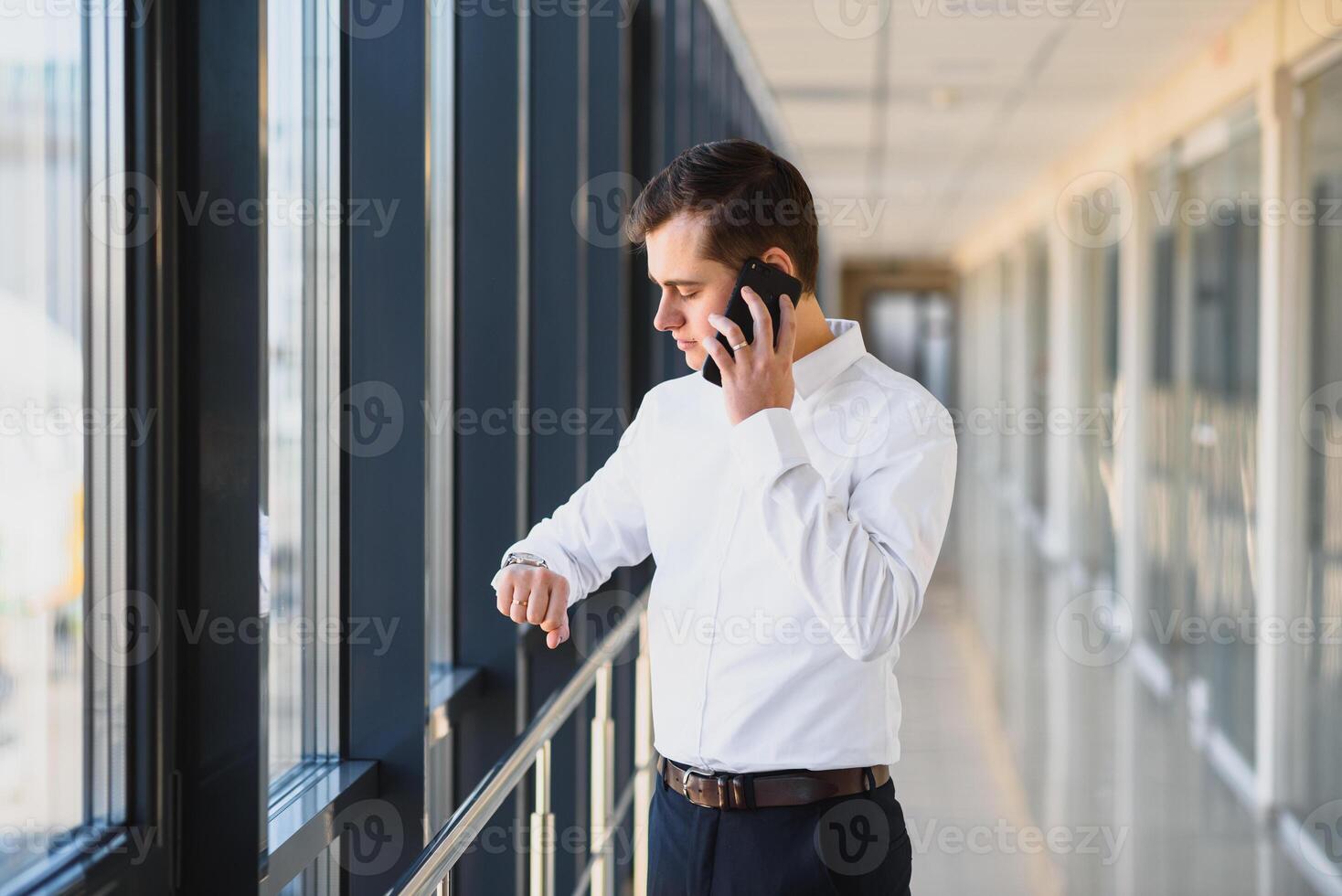 Portrait of a serious confident man boss having mobile phone conversation while resting after meeting with his partners, businessman talking on cell telephone while standing in modern space indoors photo