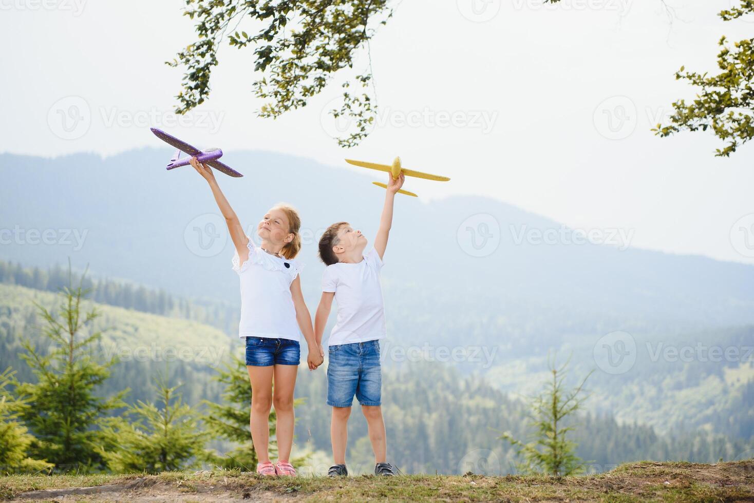Boy and girl playing with toy airplanes on a background of mountains. Happy childhood and vacation in the mountains. photo