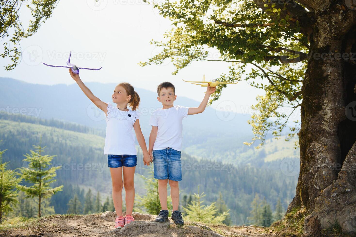 Boy and girl playing with toy airplanes on a background of mountains. Happy childhood and vacation in the mountains. photo