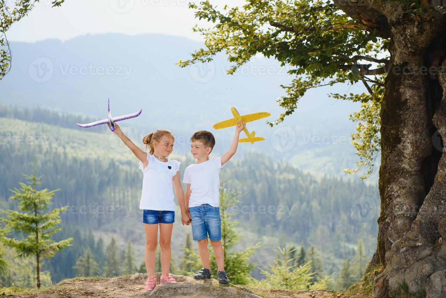 Boy and girl playing with toy airplanes on a background of mountains. Happy childhood and vacation in the mountains. photo