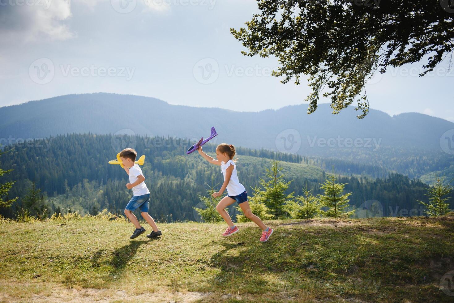 Boy and girl playing with toy airplanes on a background of mountains. Happy childhood and vacation in the mountains. photo