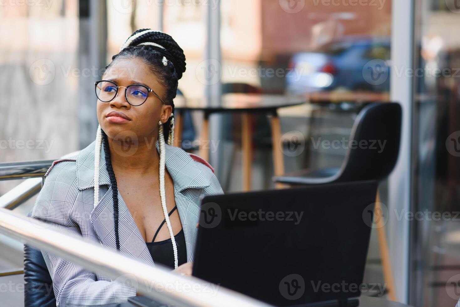 Human and technology. Young african woman typing on laptop, texting friends via social networks. Student girl browsing Internet, using free wi-fi, sitting at cafe near window on sunny day photo