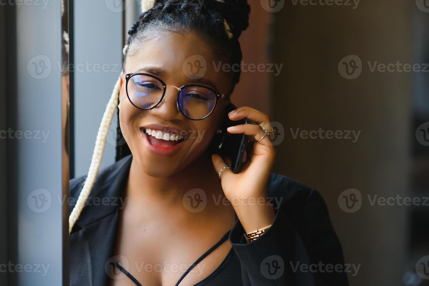 Smiling dark skinned woman in trendy wear laving cafe talking on mobile phone via roaming tariffs,african american millennial female walking and making smartphone call satisfied with connection photo