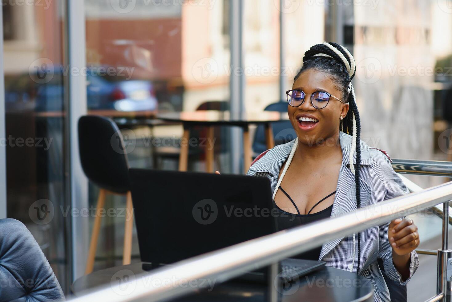 Human and technology. Young african woman typing on laptop, texting friends via social networks. Student girl browsing Internet, using free wi-fi, sitting at cafe near window on sunny day photo