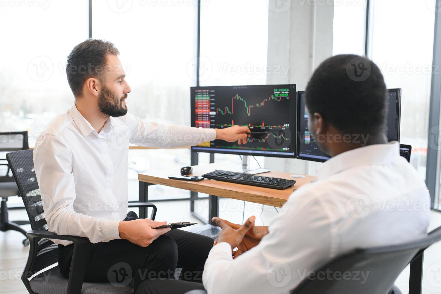 Two successful trader sitting in office, checking cryptocurrency information data on finance market graph, pointing on monitor photo