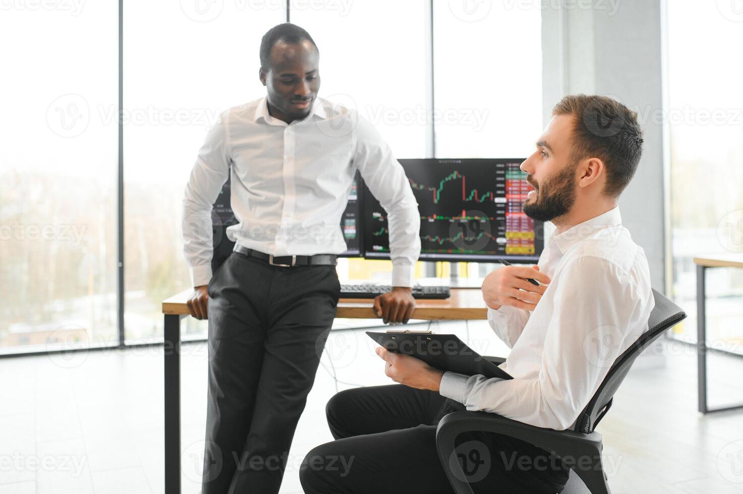 Two successful trader sitting in office, checking cryptocurrency information data on finance market graph, pointing on monitor photo
