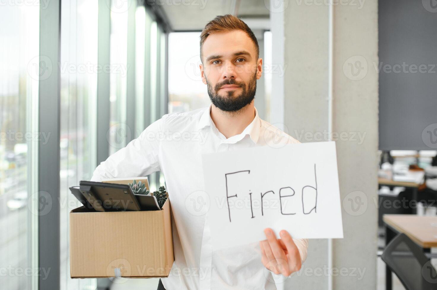 Young handsome businessman in light modern office with carton box. Last day at work. Upset office worker is fired photo