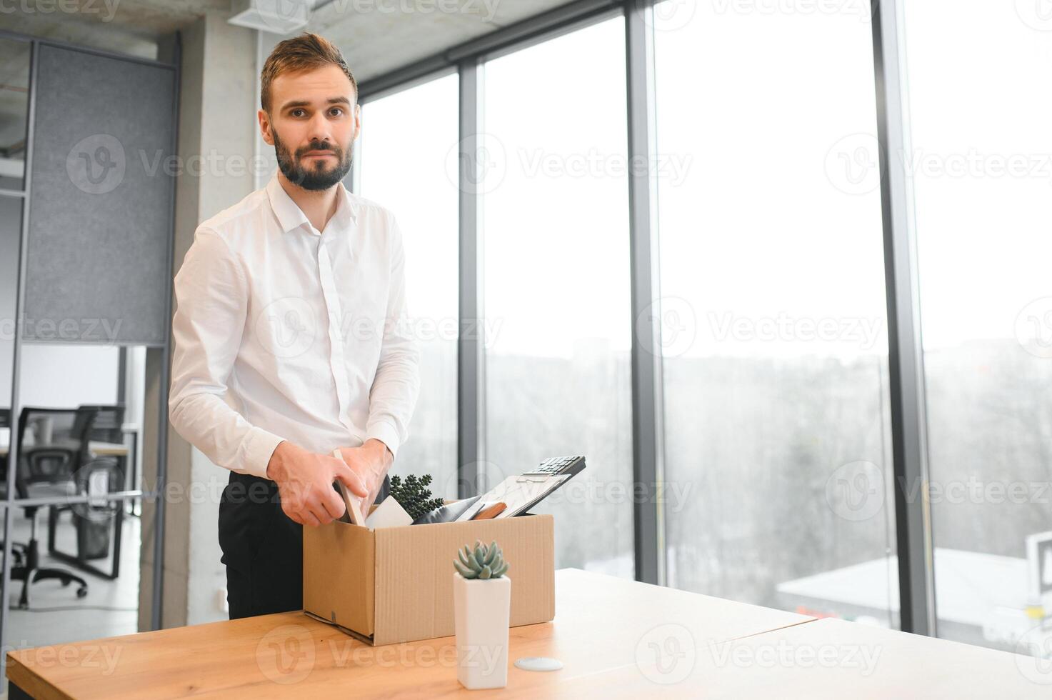 Young handsome businessman in light modern office with carton box. Last day at work. Upset office worker is fired photo