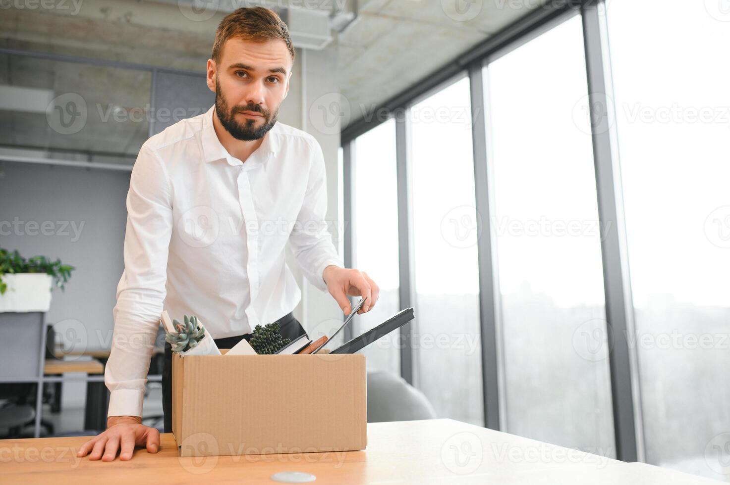 Young handsome businessman in light modern office with carton box. Last day at work. Upset office worker is fired photo