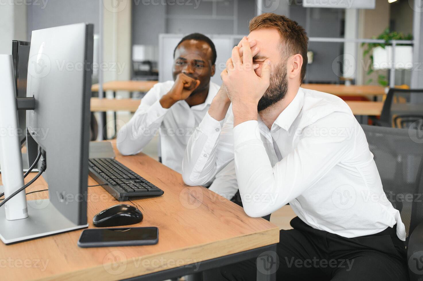 Two Unhappy tired businessman, corporate manager, sits at the workplace, tired from online work, stressed, nervous, massages the bridge of his nose, closed his eyes, experiencing a headache photo