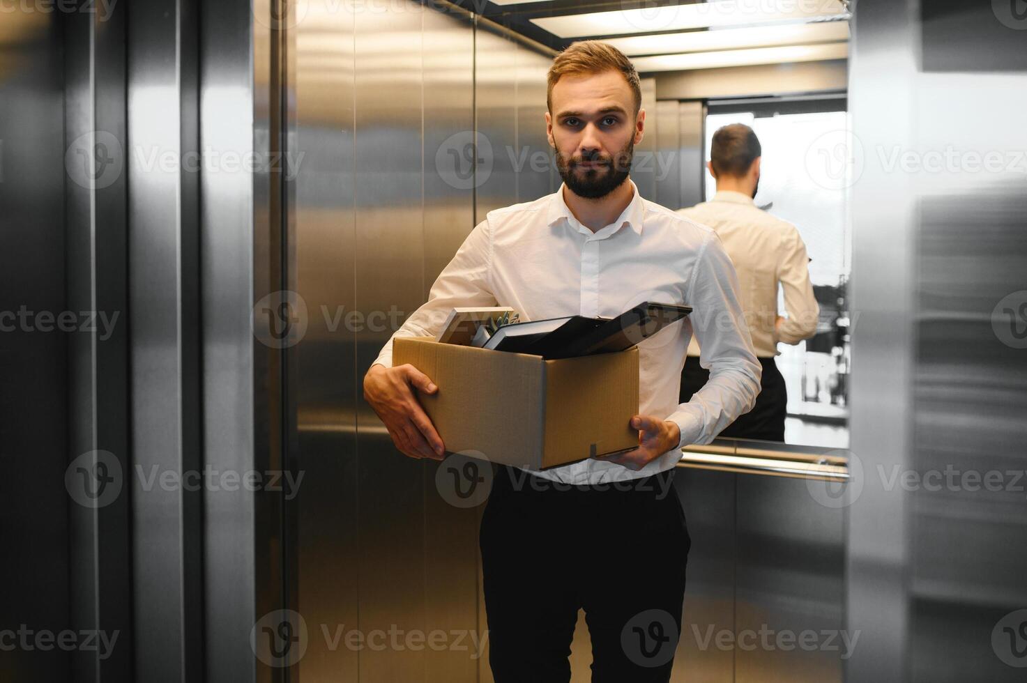 Young handsome businessman in light modern office with carton box. Last day at work. Upset office worker is fired photo