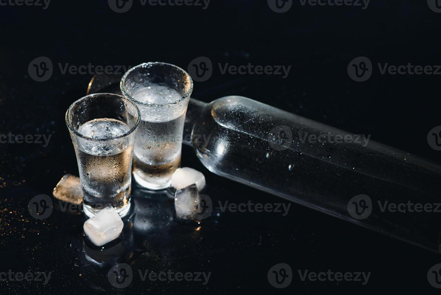 Close-up view of bottle and glasses of vodka standing isolated on black. photo