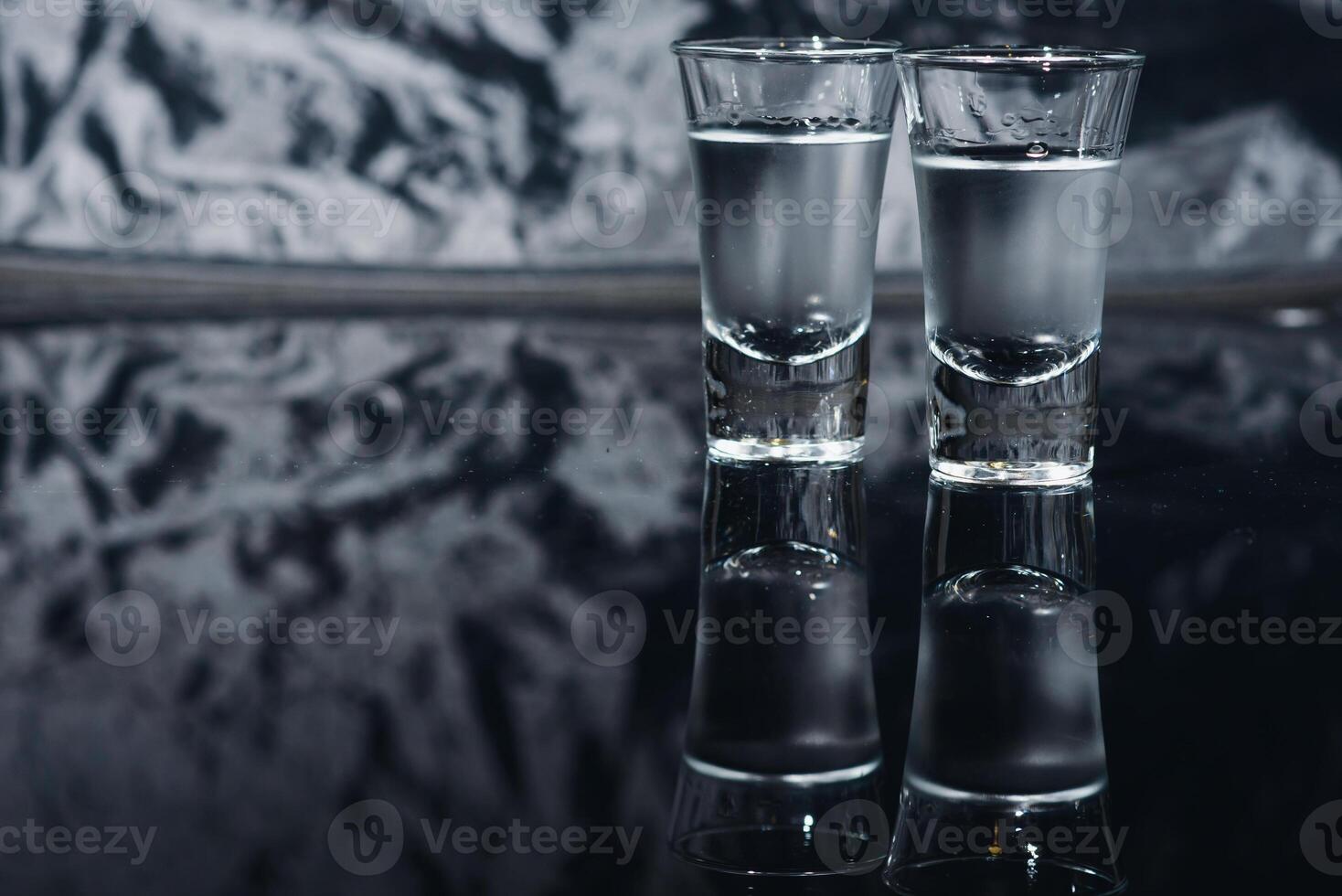 Close-up view of bottle of vodka with glasses standing on ice on black. photo