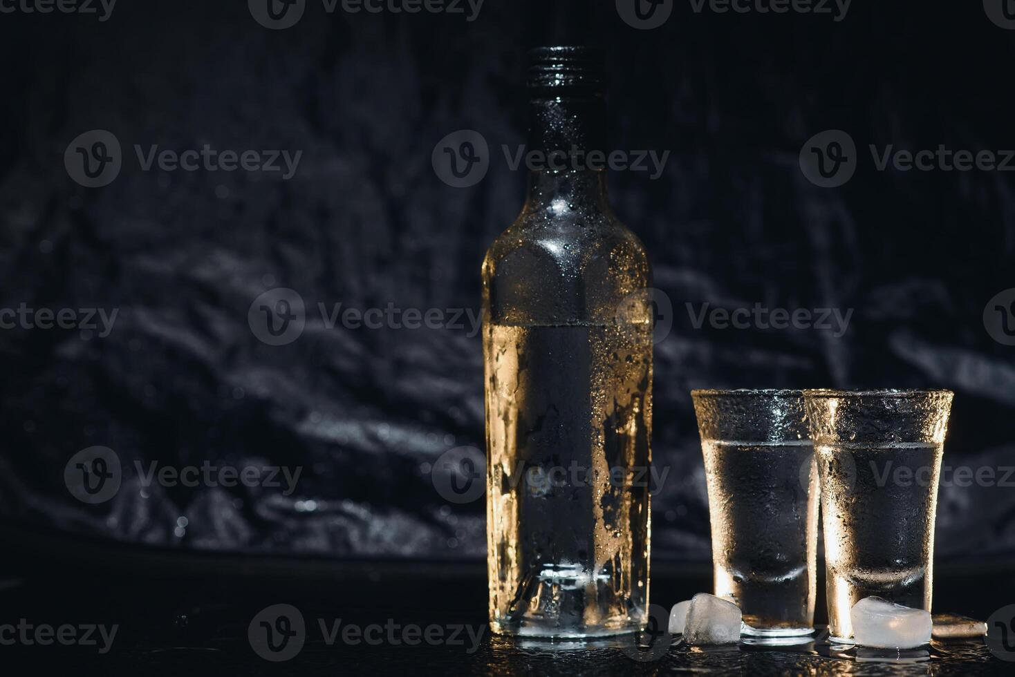 Close-up view of bottle of vodka with glasses standing on ice on black. photo