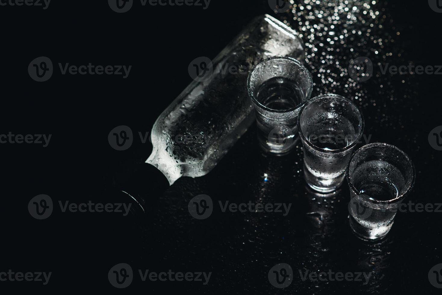 Vodka in shot glasses on black background, iced strong drink in misted glass. photo