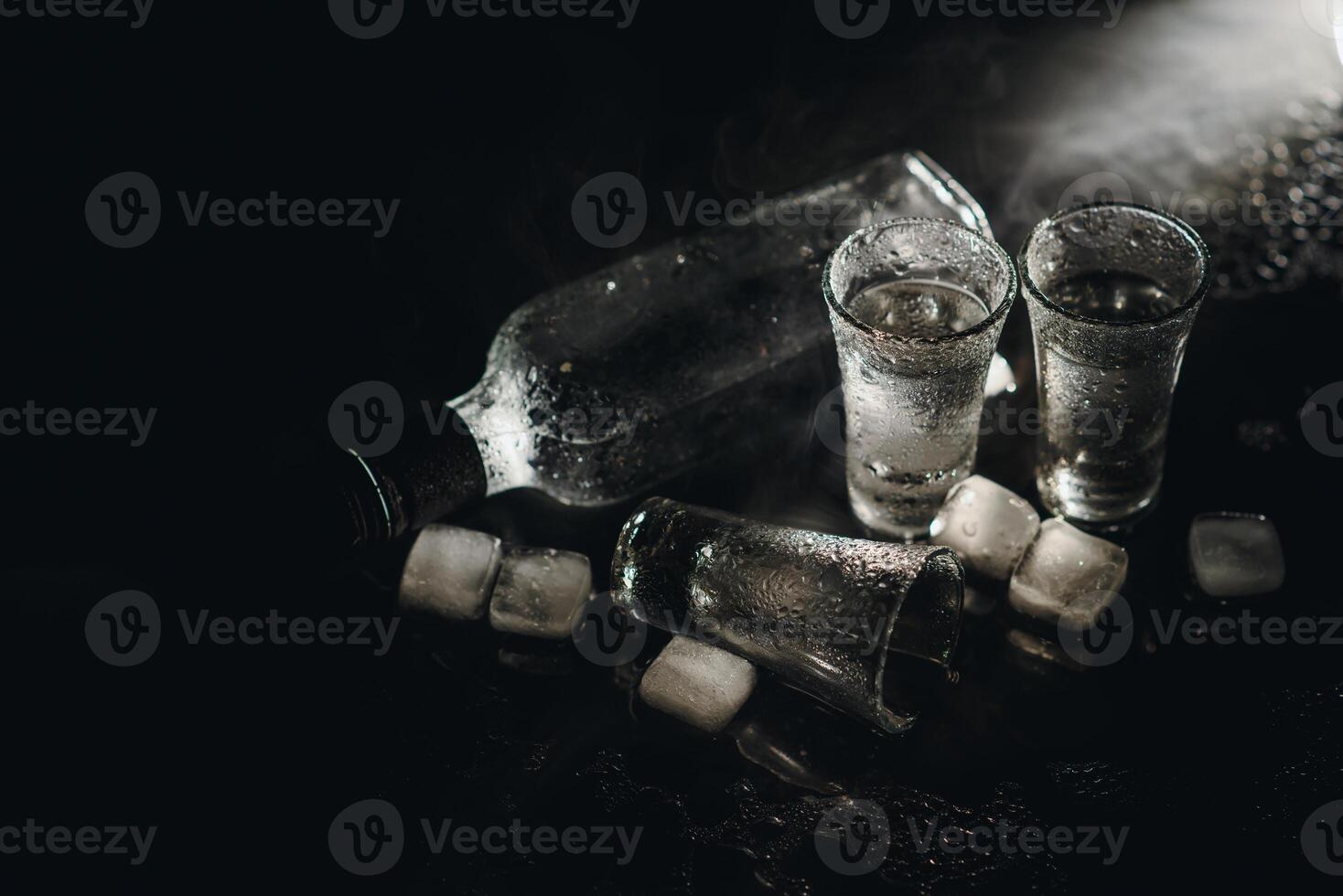 Close-up view of bottle of vodka with glasses standing on ice on black. photo