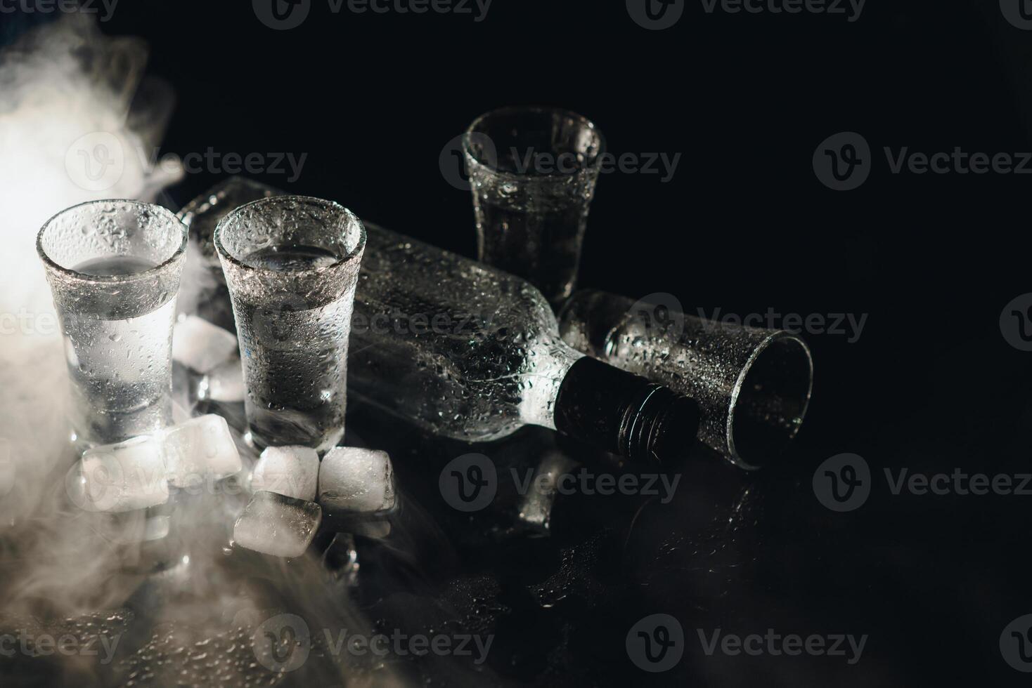 Close-up view of bottle and glasses of vodka standing isolated on black. photo