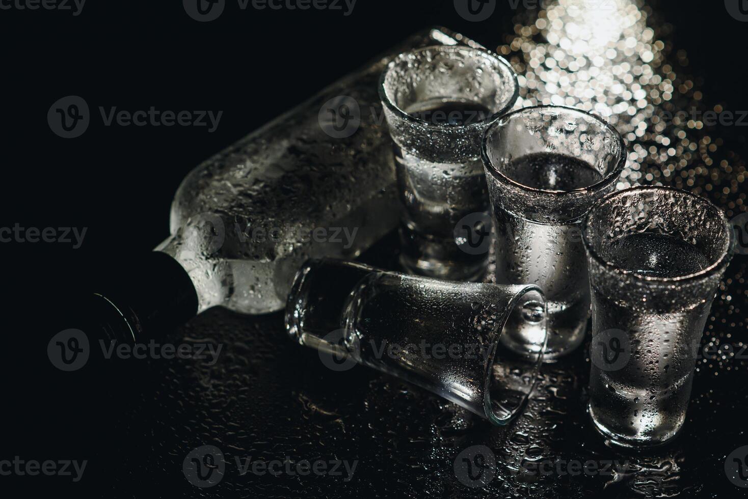 Vodka in shot glasses on black background, iced strong drink in misted glass. photo