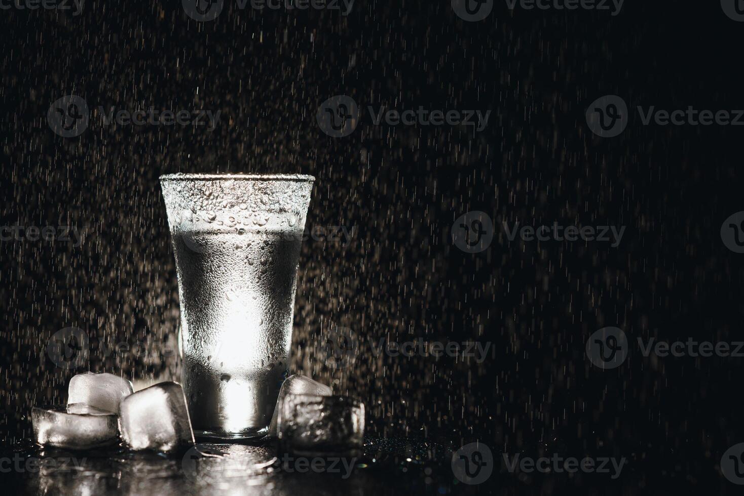 Close-up view of bottle of vodka with glasses standing on ice on black. photo
