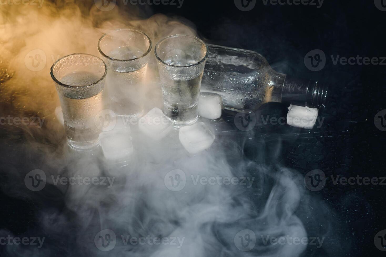 Close-up view of bottle and glasses of vodka standing isolated on black. photo