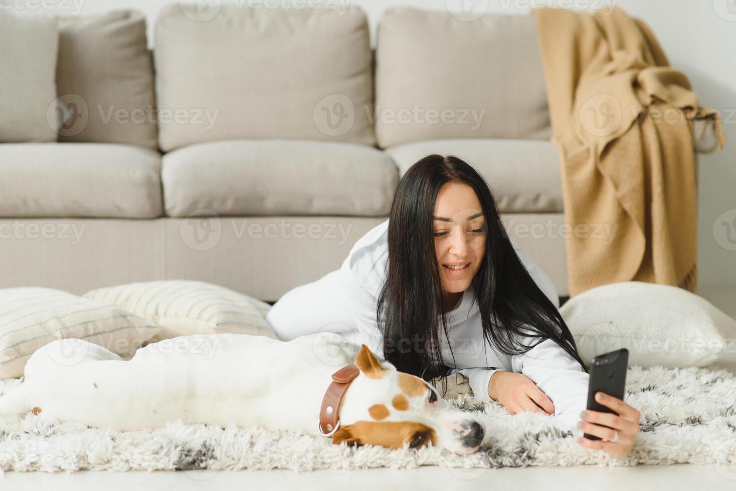 Portrait of beautiful young woman with her dog using mobile phone at home photo