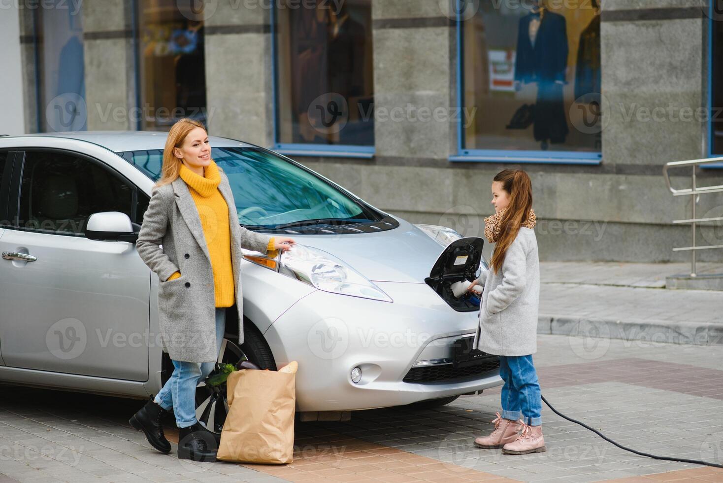 Stylish mother and daughter charge an electric car, and spend time together. photo