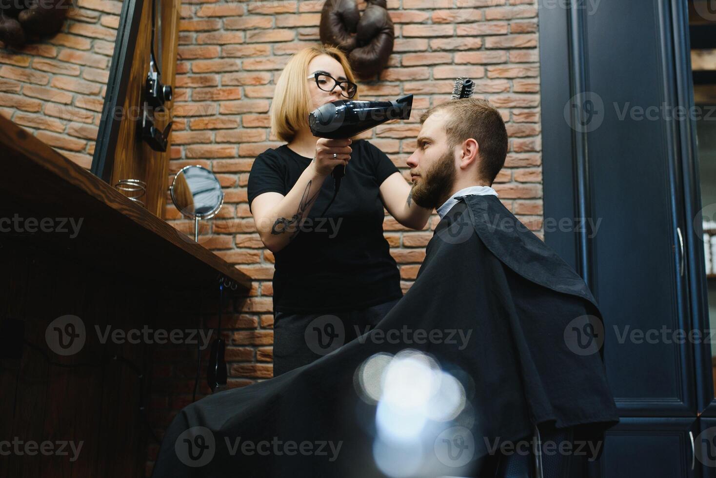 Stylish man sitting barber shop Hairstylist Hairdresser Woman cutting his hair Portrait handsome happy young bearded caucasian guy getting trendy haircut Attractive barber girl working serving client photo