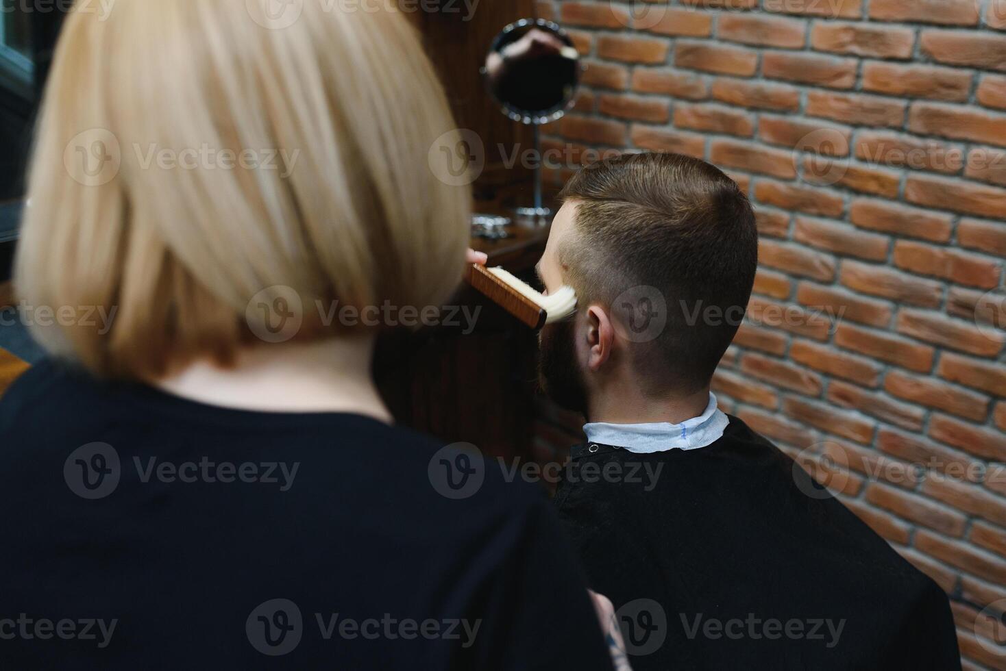 Serving client in Barbershop. Professional barber girl, female hairdresser making modern haircut for a man sitting in barber shop chair. Focus on a girl. Hairdressing, shaving, trimming, grooming photo