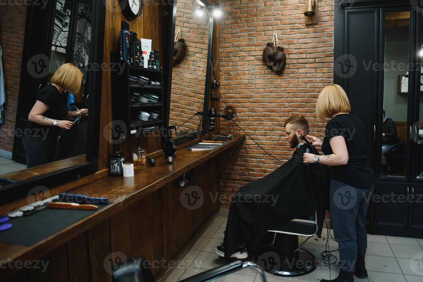 Professional hairdresser woman doing styling of handsome guy with electric hair clipper at barber shop photo
