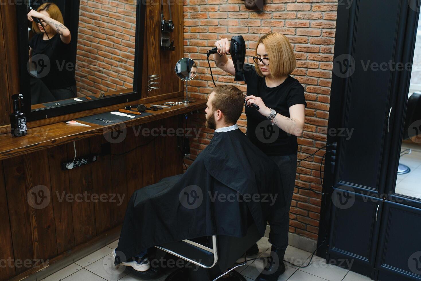 Stylish man sitting barber shop Hairstylist Hairdresser Woman cutting his hair Portrait handsome happy young bearded caucasian guy getting trendy haircut Attractive barber girl working serving client photo