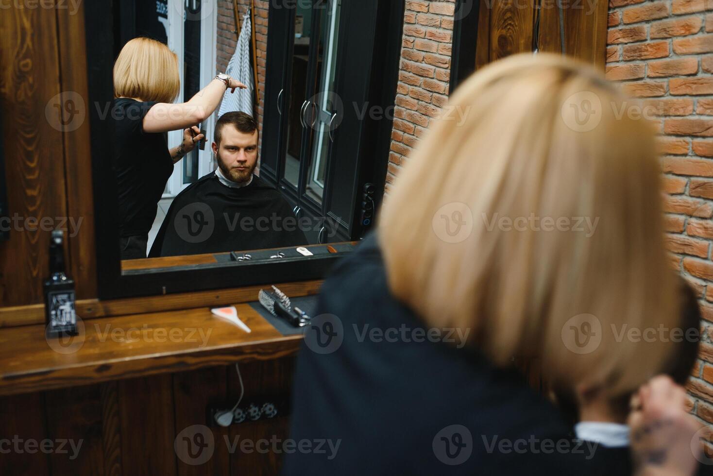 Stylish man sitting barber shop Hairstylist Hairdresser Woman cutting his hair Portrait handsome happy young bearded caucasian guy getting trendy haircut Attractive barber girl working serving client photo