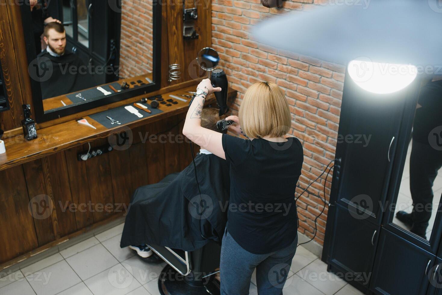 Stylish man sitting barber shop Hairstylist Hairdresser Woman cutting his hair Portrait handsome happy young bearded caucasian guy getting trendy haircut Attractive barber girl working serving client photo