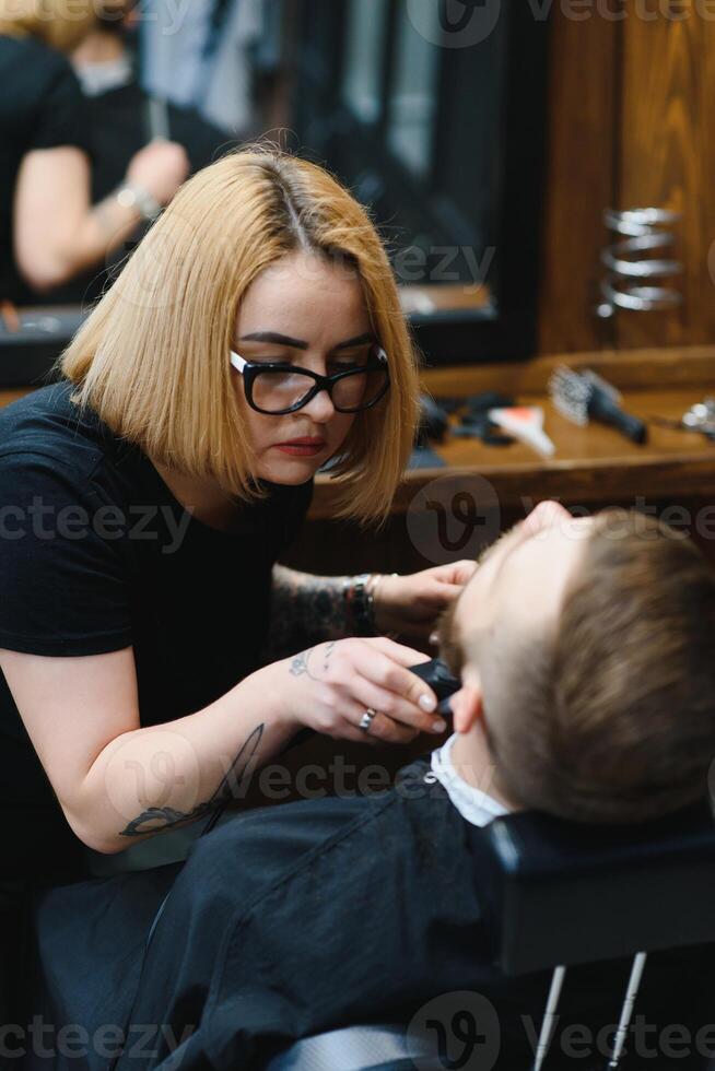 Barbershop or hairdresser concept. Woman hairdresser cuts beard with scissors. Man with long beard, mustache and stylish hair. Guy with modern hairstyle visiting hairdresser photo