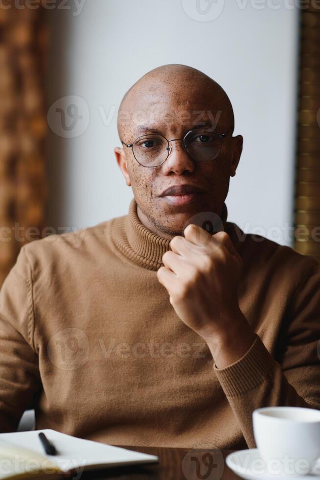 African-Ameican entrepreneur wearing shirt with rolled up sleeves looking through window with thoughtful and serious face expression, feeling nervous before meeting with business partners at cafe. photo