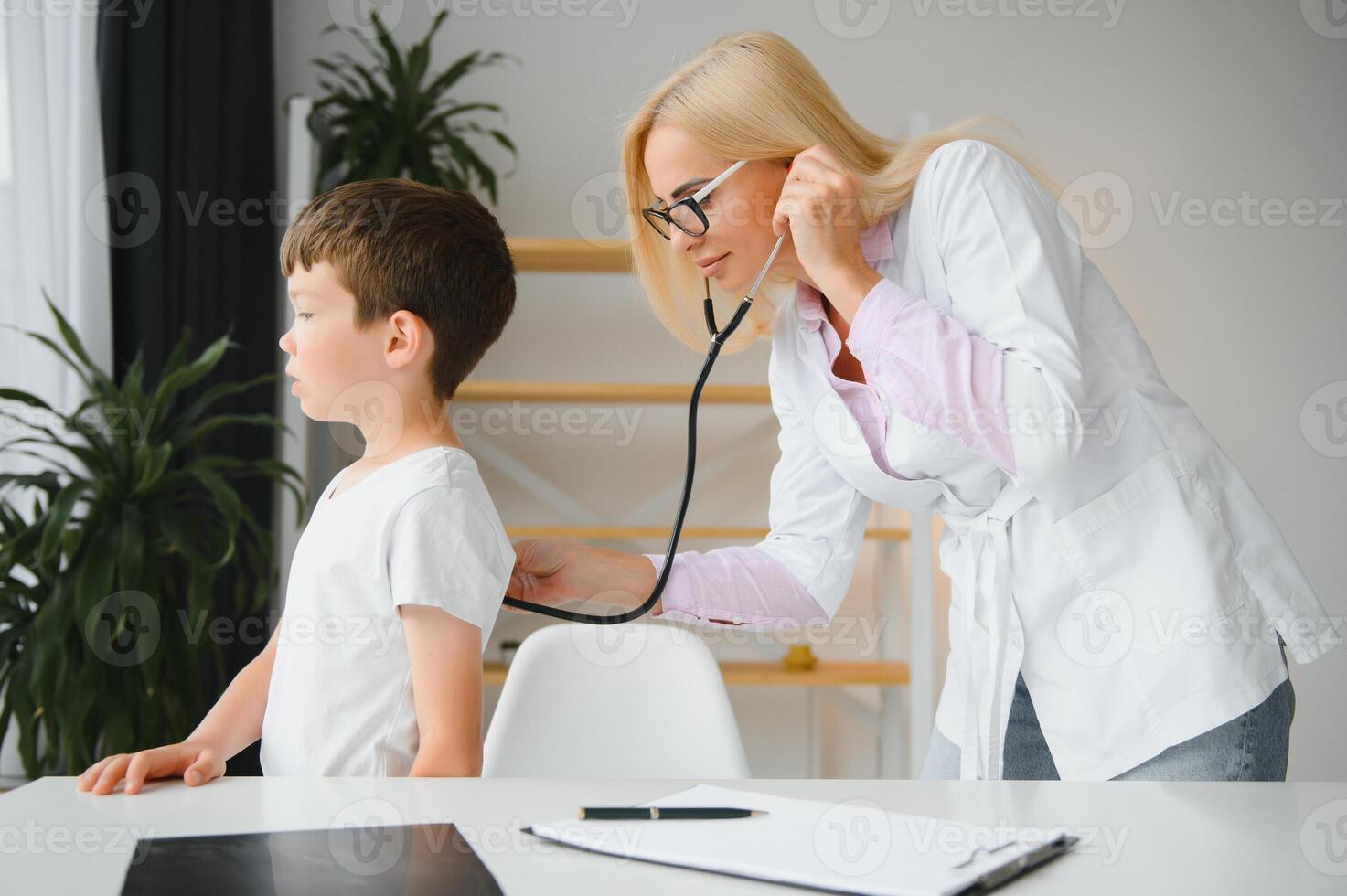 Pediatrician listening to breathing in the lungs and heartbeat with stethoscope. Portrait of adorable little boy visiting doctor. photo